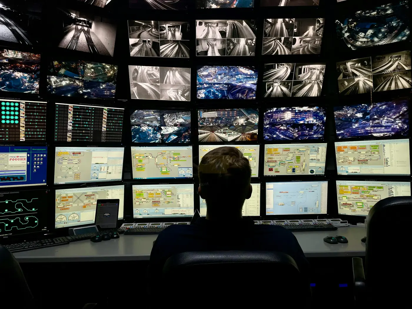 A person at a desk facing a wall of security monitors