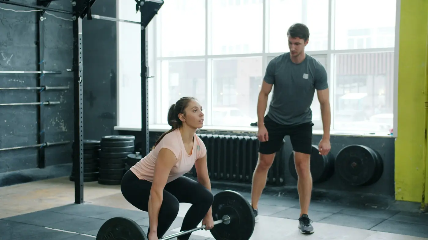 A woman lifting weights while a trainer watches her form