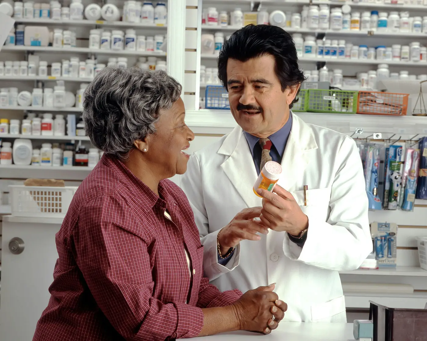 A pharmacist in a white coat showing a pill bottle to a customer