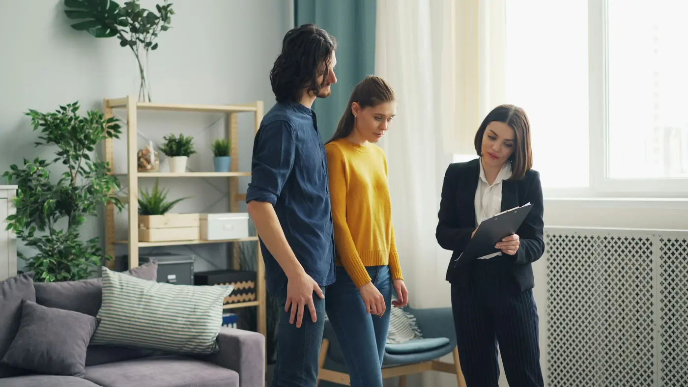 A real estate agent with a clipboard talking with a couple in a bright living room